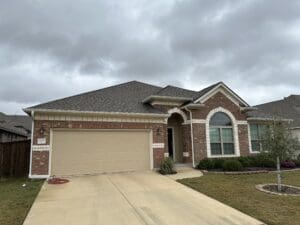 A brick house with a two-car garage under a cloudy sky.