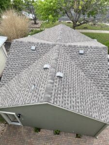 A gray shingled rooftop with multiple vents and a green yard surrounding it.