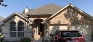 A suburban brick house with a gray roof and a car parked outside.