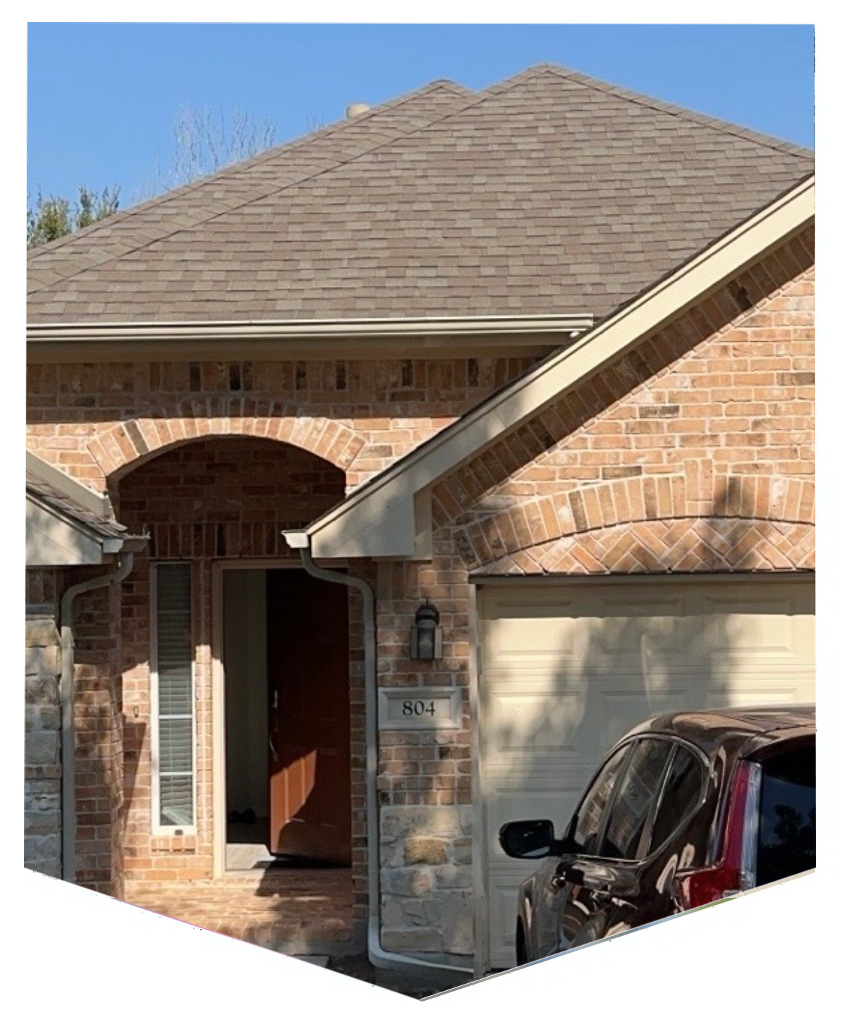 Brick house entrance with an open door and a parked car.