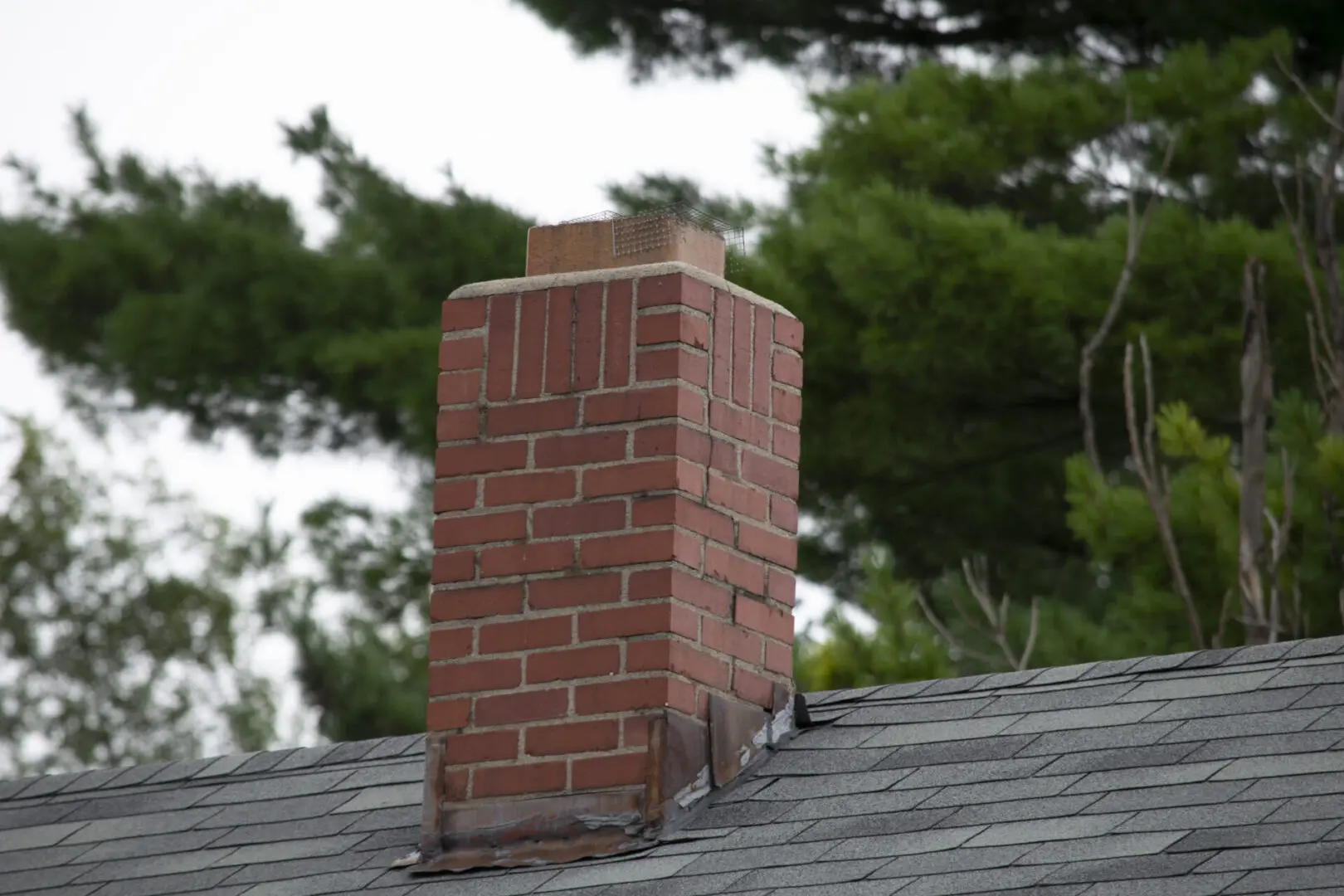 A brick chimney on a rooftop with greenery in the background.